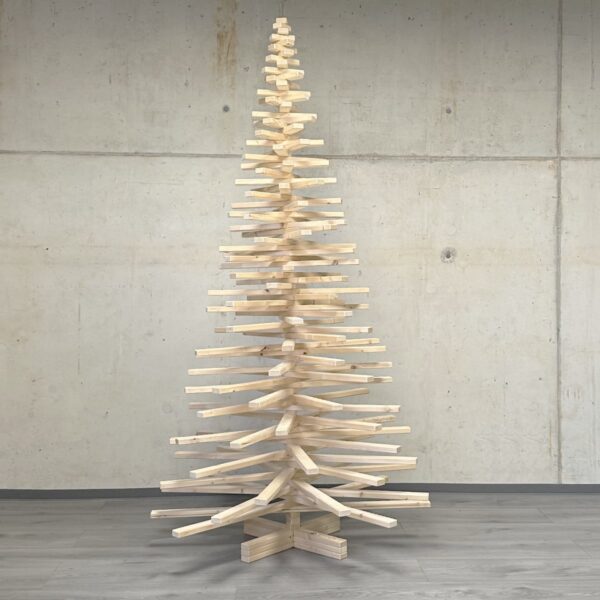 Moderner Holzweihnachtsbaum in minimalistischer Aufmachung, handgefertigt aus nachhaltigem Kiefernholz, vor einer Betonwand.
