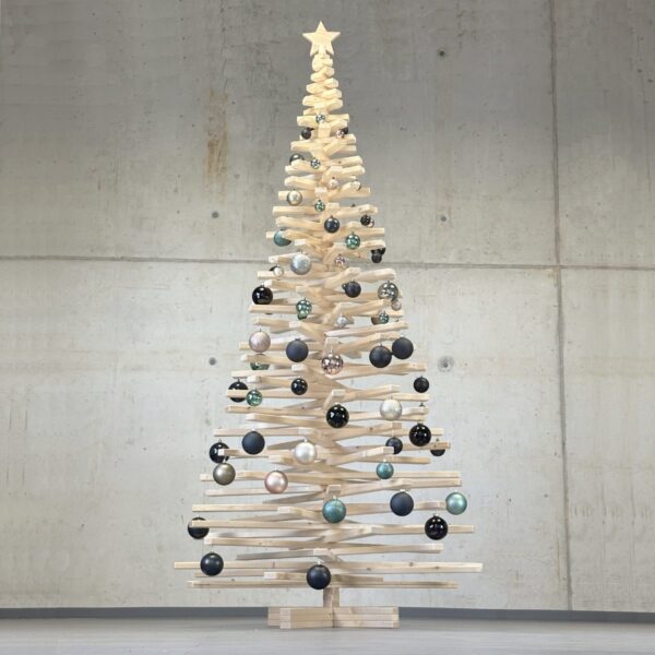 Xtra Franky (220 cm) aufgedreht und geschmückt mit eleganten Kugeln, einem Holzstern als Spitze und vor einer Betonwand platziert