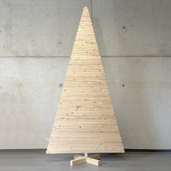 Großer Holzweihnachtsbaum in traditioneller Dreiecksform vor einer Betonwand, handgefertigt aus nachhaltigem Kiefernholz.