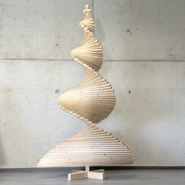 Spiralartig gedrehter Holzweihnachtsbaum aus Kiefernholz vor einer Betonwand, handgefertigt und modern gestaltet.