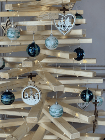 Eine Nahaufnahme eines nachhaltigen Weihnachtsbaums aus Holz mit blauen und weißen Kugeln geschmückt vor einer weißen Wand.