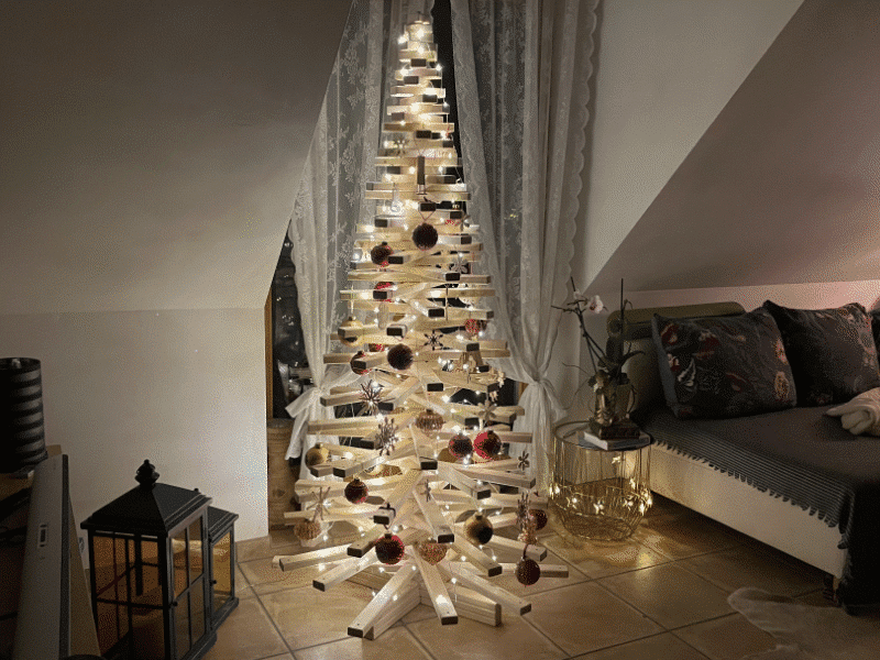 ein Wohnzimmer mit einem traditionell geschmückten Weihnachtsbaum, einer Nordmanntanne. Mit Kerzen, Kugeln und Geschenken dekoriert