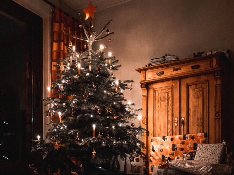 ein Wohnzimmer mit einem traditionell geschmückten Weihnachtsbaum, einer Nordmanntanne. Mit Kerzen, Kugeln und Geschenken dekoriert