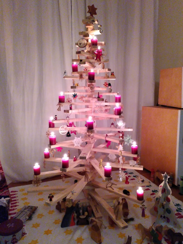 Dekorierter Christbaum aus Fichtenholz vor einem Fenster, beleuchtet mit einer Lichterkette