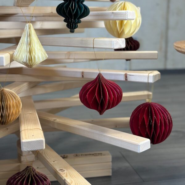 Nahaufnahme eines Large Franky Holzweihnachtsbaumes, geschmückt mit Papieranhängern in Wabenstruktur in warmen Farben wie Rot, Weiß und Gold.