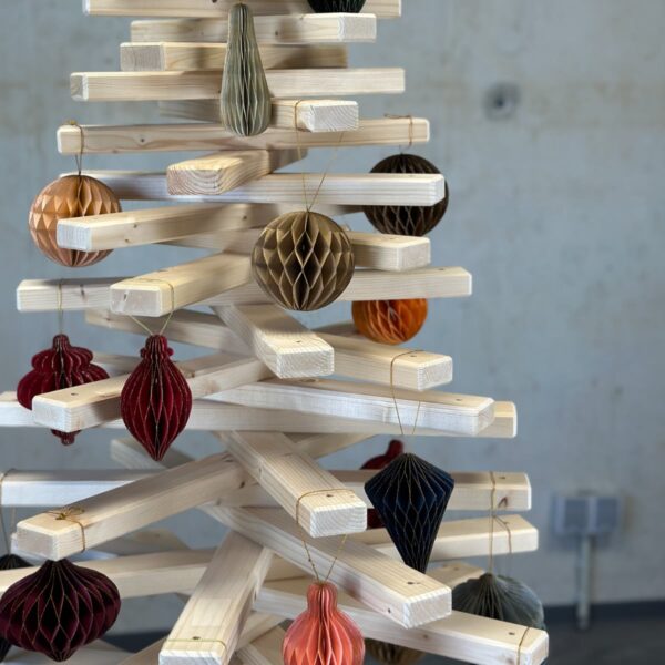 Detailaufnahme eines Large Franky Holzweihnachtsbaumes, geschmückt mit nachhaltigen Papieranhängern in Wabenstruktur und warmen, nostalgischen Farben.