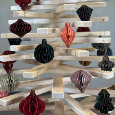 Nahaufnahme eines Large Franky Holzweihnachtsbaumes, dekoriert mit nachhaltigen Papieranhängern in Wabenstruktur in nostalgischen Farben.