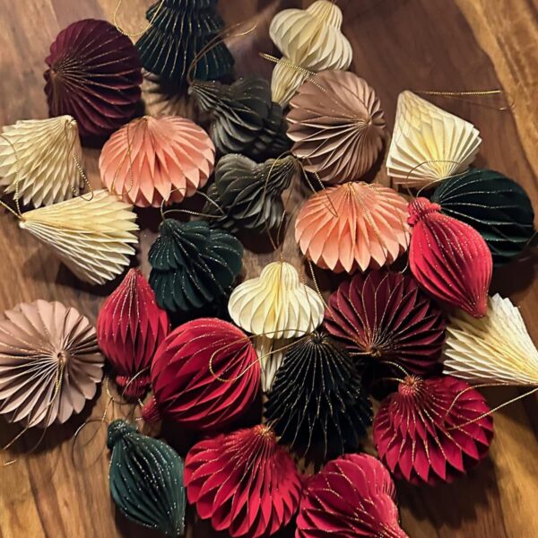 Eine Sammlung von nachhaltigen Papieranhängern in Wabenstruktur in festlichen Farben wie Rot, Grün, Beige und Gold, arrangiert auf einem Holztisch.